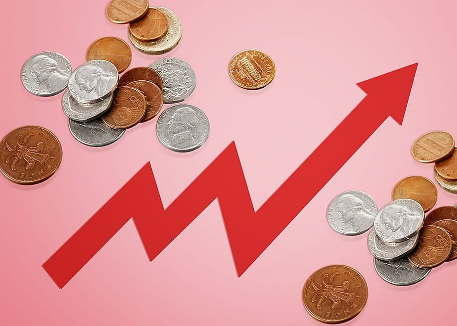 Rising arrow to depict rising costs against a background of coins. — Billion Photos // Shutterstock