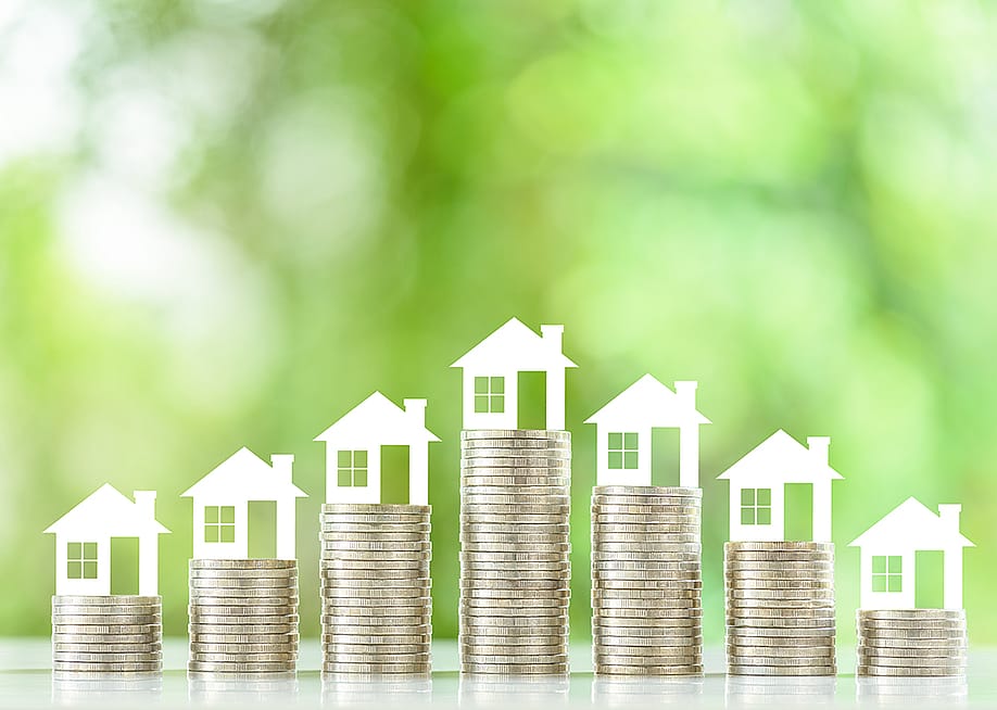 Tiny figures of residential houses atop coin stacks. — William Potter // Shutterstock