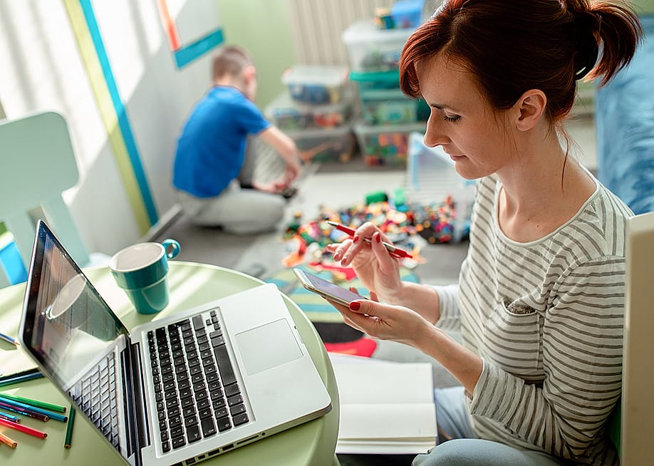 Mother working from home with a laptop and phone. — Zoran Zeremski // Shutterstock