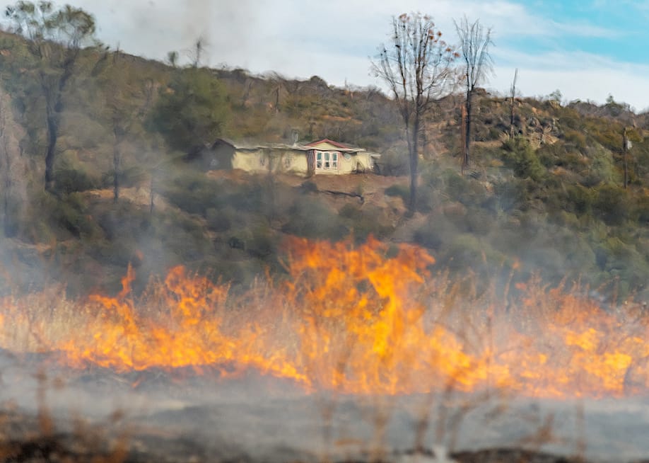 A wildfire blurs the view of a home from a distance. — Elkins Eye Visuals // Shutterstock