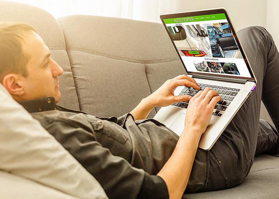 Man lying on sofa while using his laptop to browse for cars online. — Andrew Angelov // Shutterstock