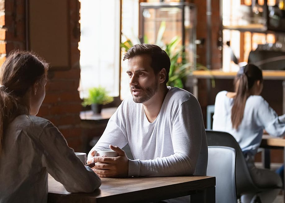 Millenial couple sitting at a cafe table engaged in discussion. — fizkes // Shutterstock