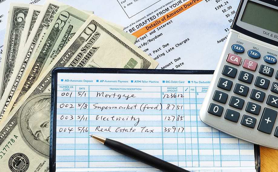 Balancing a checkbook with U.S. bills and calculator and bills visible on a table. — JohnKwan // Shutterstock