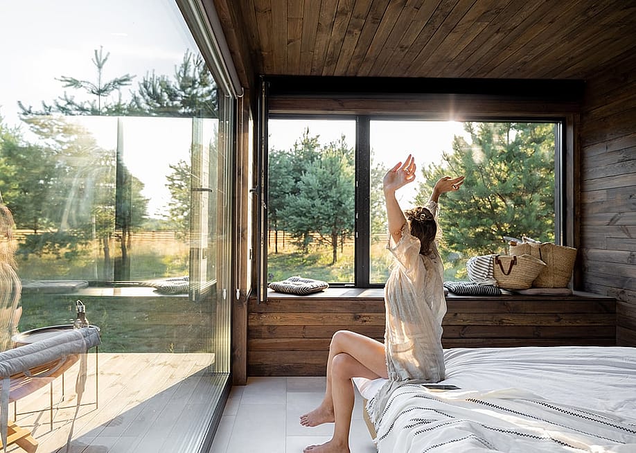 Woman stretching as she is waking up in a modern country house with glass windows. — RossHelen // Shutterstock