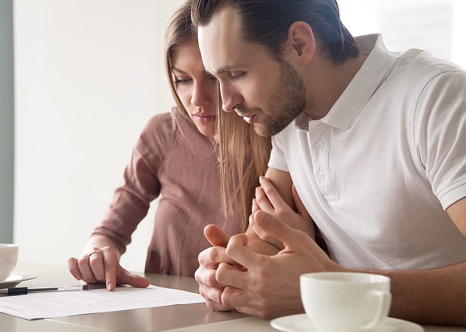 Two people looking over paperwork carefully, lit by window light during the daytime. — fizkes // Shutterstock