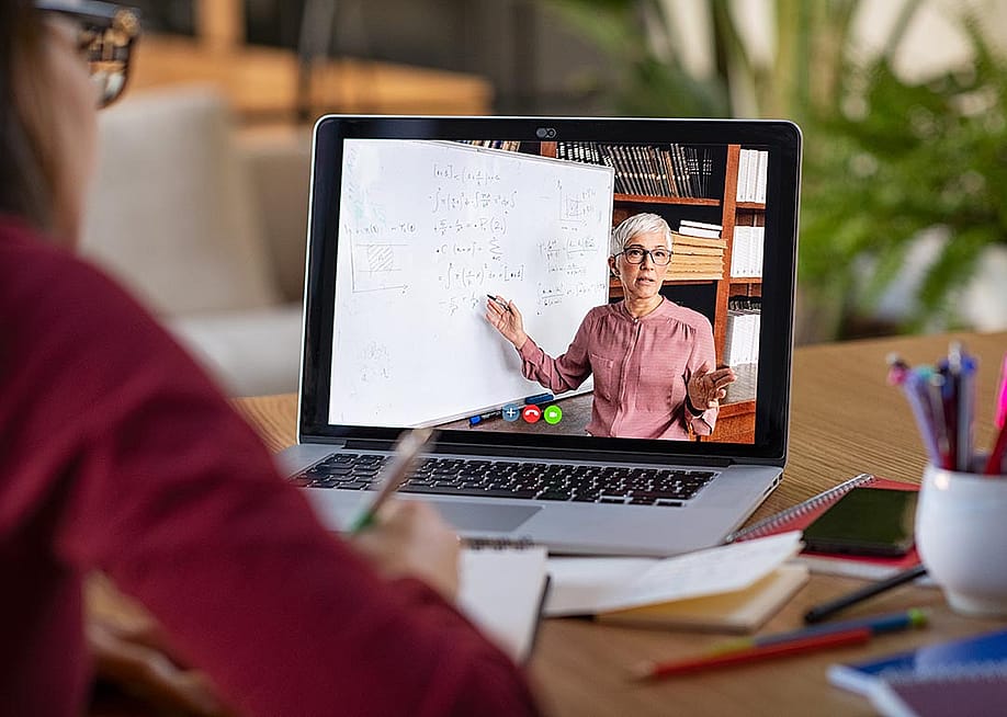 A video on a computer screen video showing an older teacher demonstrating lesson on whiteboard, with student watching in foreground. — Ground Picture // Shutterstock