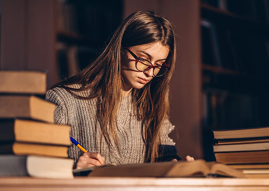 Young female student studying with a pile of books beside her. — bedya // Shutterstock