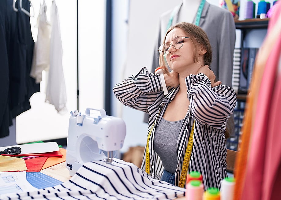 A tailoring shop owner holding the back of her neck from being tired and stressed. — Krakenimages.com // Shutterstock
