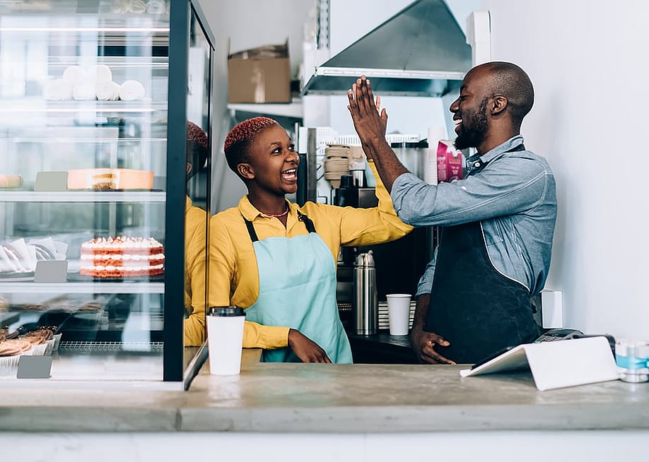 Cheerful black business owners giving high five to each other behind their store counter. — GaudiLab // Shutterstock