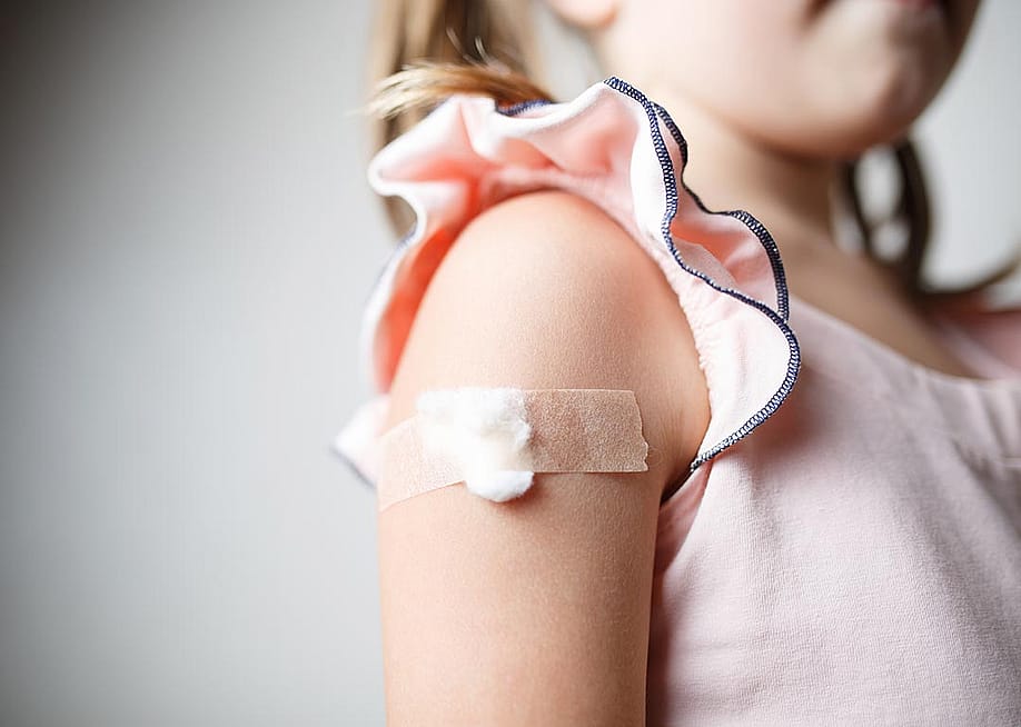 Close up of child's upper arm with a cotton ball and tape covering vaccination site. — Alexxndr // Shutterstock