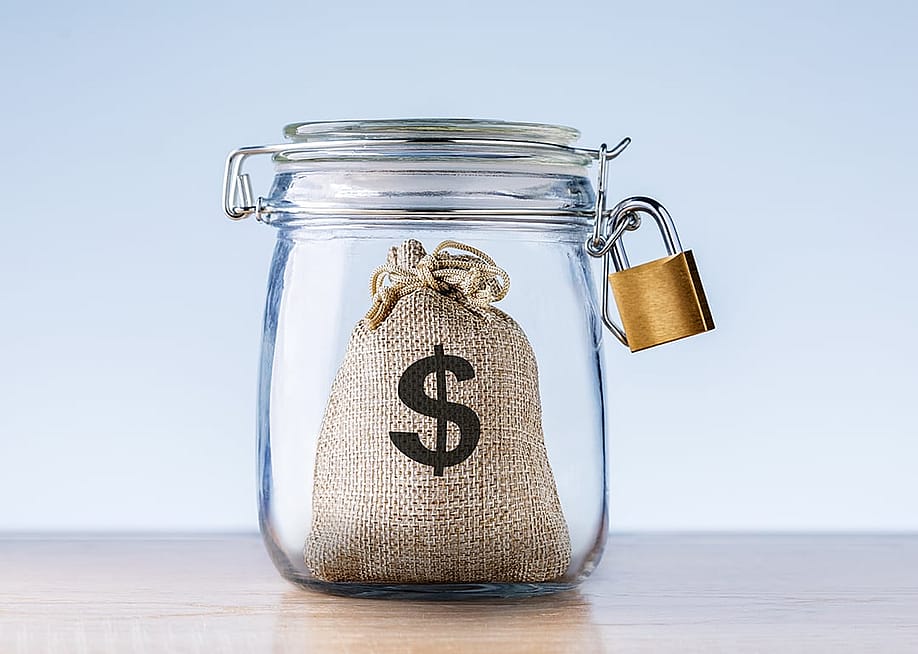 Concept of an emergency fund - a mini bag with a dollar symbol on it locked inside a jar. — CHUYKO SERGEY // Shutterstock