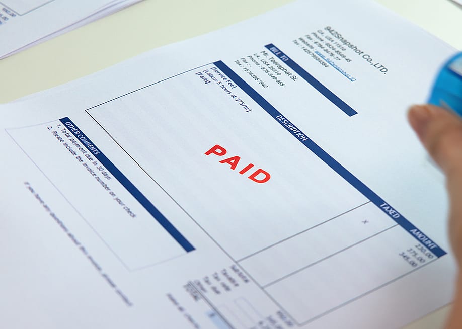 Worker sealing "paid" sign on an invoice document. — Chay_Tee // Shutterstock