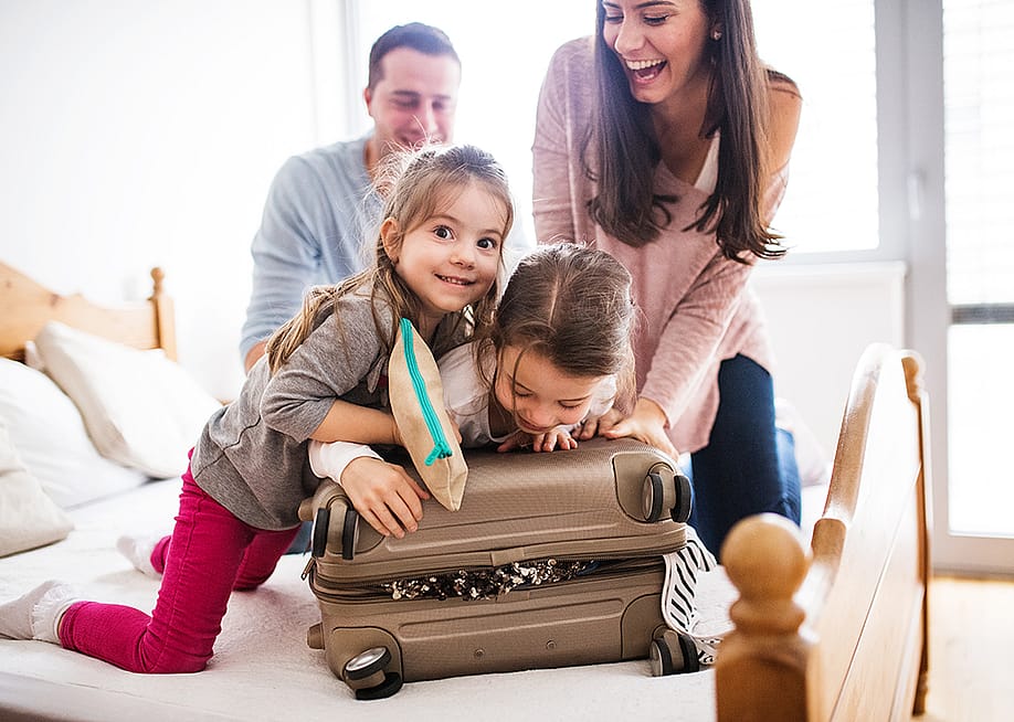 A happy family trying to close a packed suitcase. — Ground Picture // Shutterstock