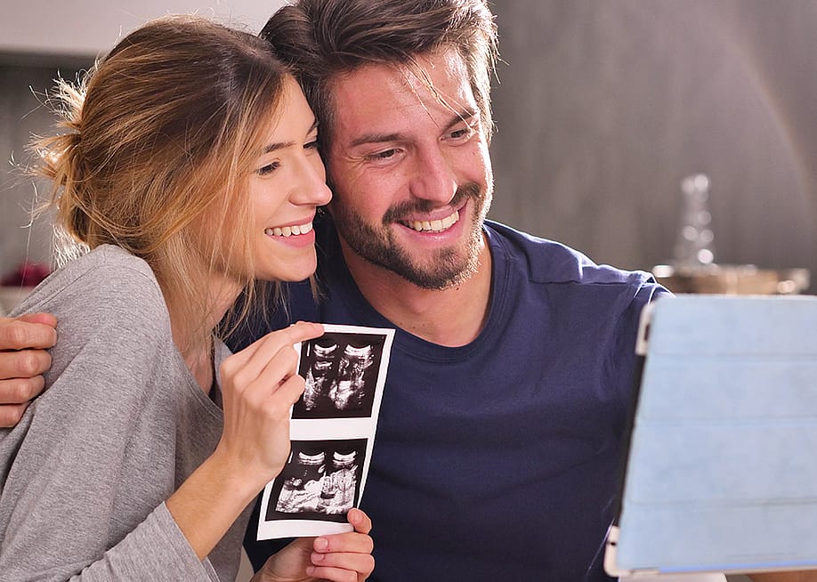 A young couple sharing ultrasound photographs while in a virtual call with loved ones. — Kitreel // Shutterstock