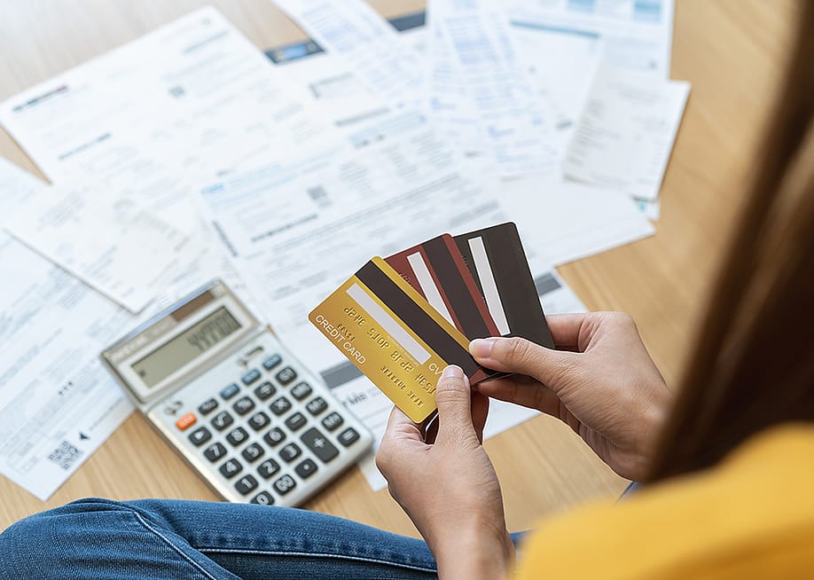 Young woman holding several credit cards and calculating a pile of bills. — Pormezz // Shutterstock