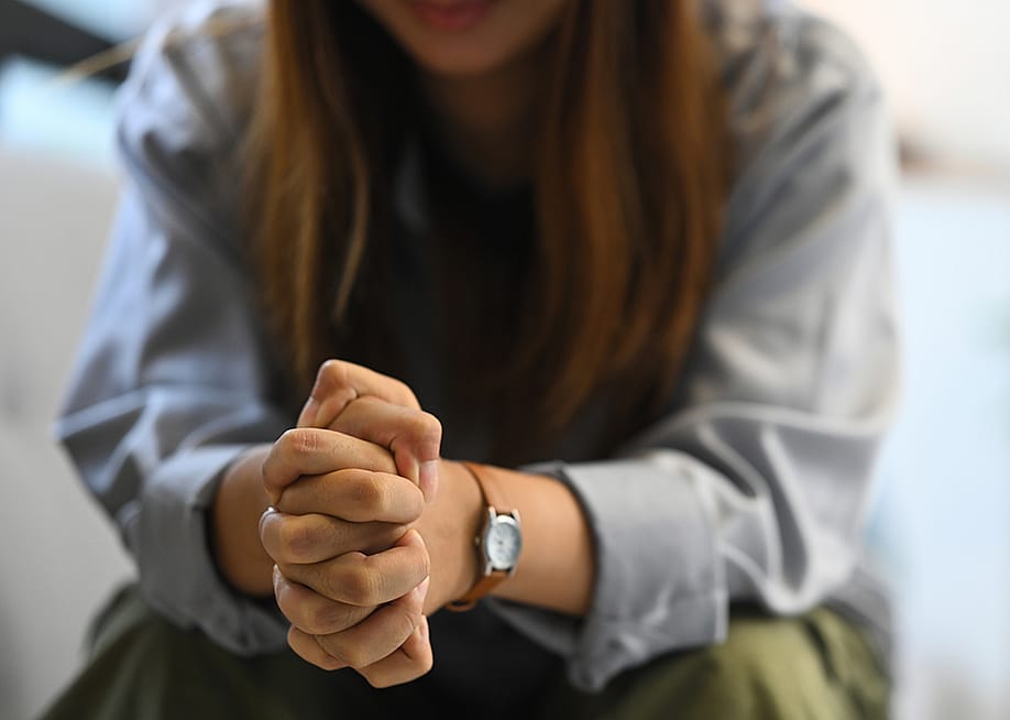 Sad woman sitting on a sofa with hands clasped. — Prathankarnpap // Shutterstock