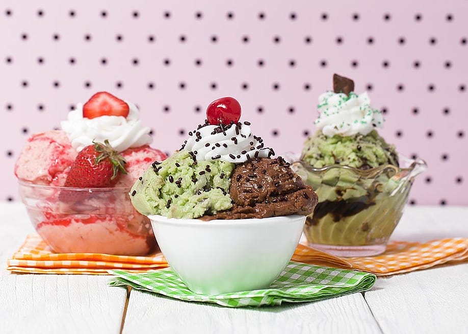 Three bowls of ice cream including strawberry, pistachio and chocolate with whipped cream and different toppings. — Dan Kosmayer // Shutterstock