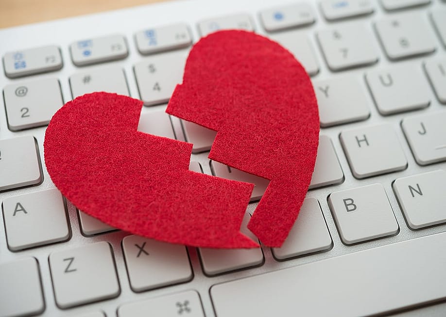 A red broken heart cutout on top of a white keyboard. — Pla2na // Shutterstock