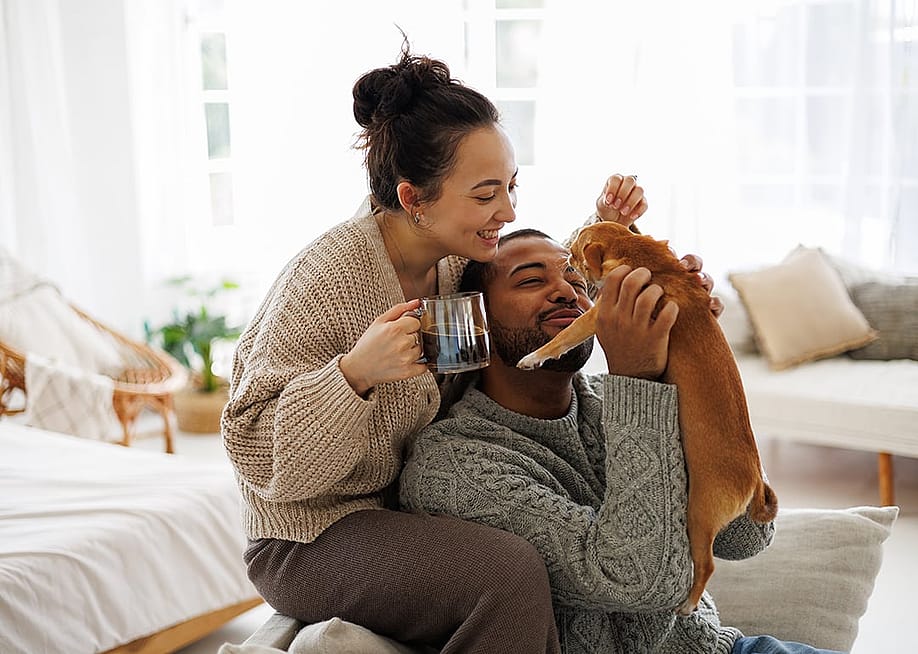 Happy couple at home playing with their dog. — Dmytro Hai // Shutterstock