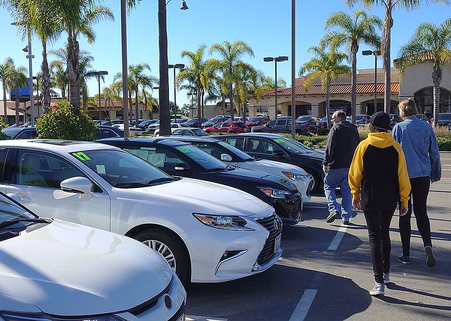 A parent and his teenagers looking at a row of used cars. — Simone Hogan // Shutterstock
