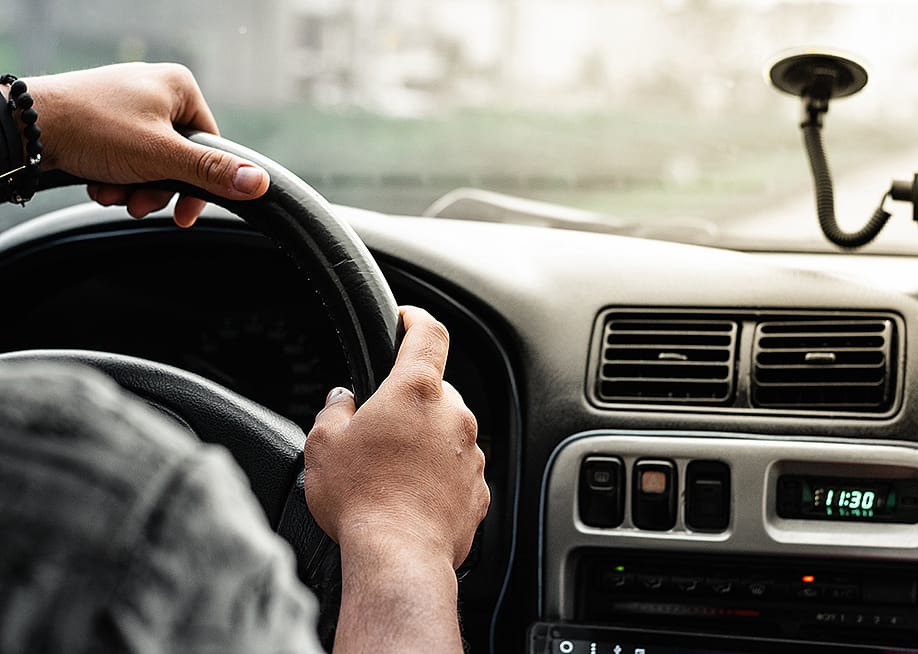 Close-up of a man holding the steering wheel while driving on the road. — Maurotoro // Shutterstock