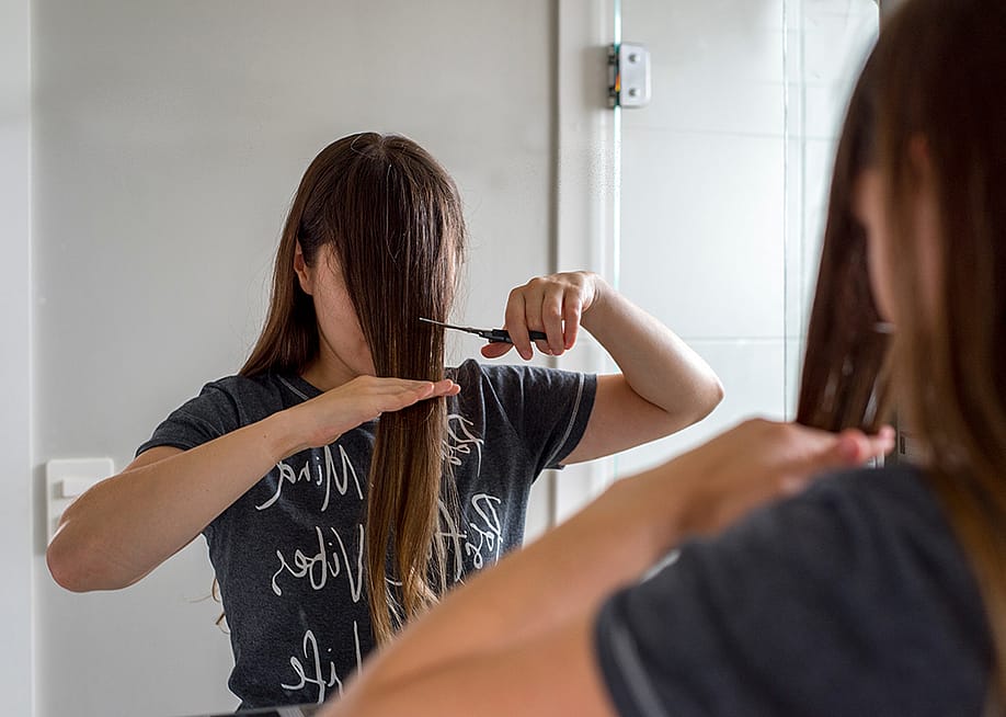 A woman cuts her hair in front of a mirror to have bangs. — M M Vieira // Shutterstock