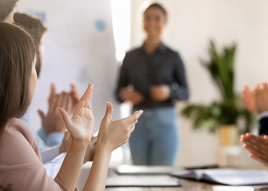 Members of a team applaud another member after a successful meeting presentation. — fizkes // Shutterstock