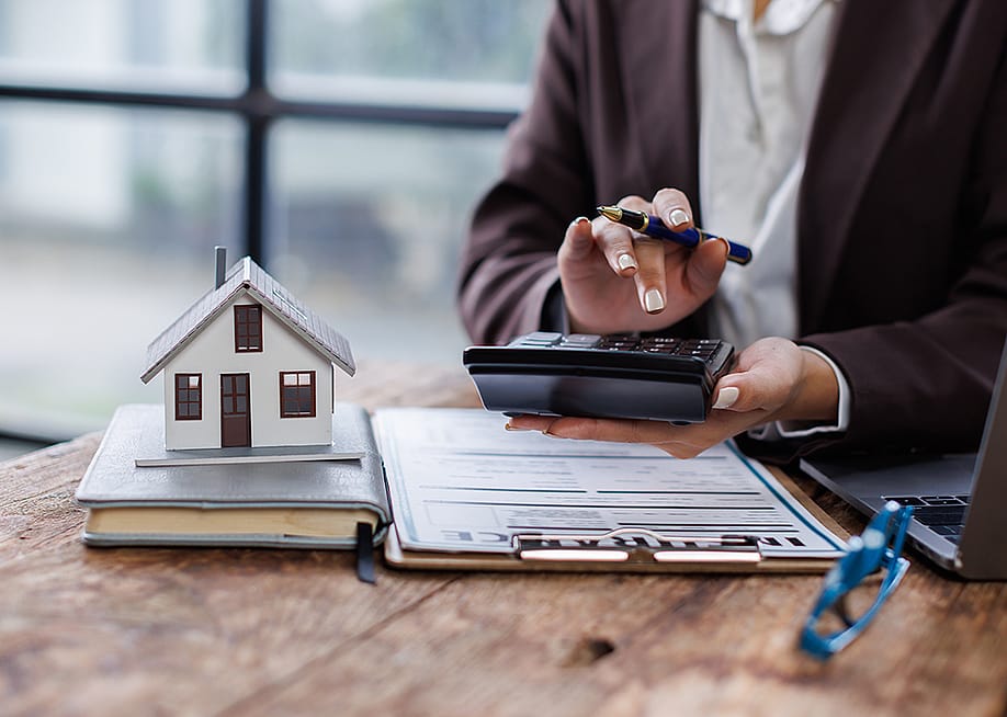 Property agent calculating taxes with a figure of a house and contract on a table. — David Gyung // Shutterstock