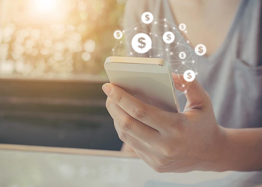 Hand holding mobile phone with dollar sign icons overlaid, symbolizing ecommerce transactions made on smartphones. — Monster Ztudio // Shutterstock