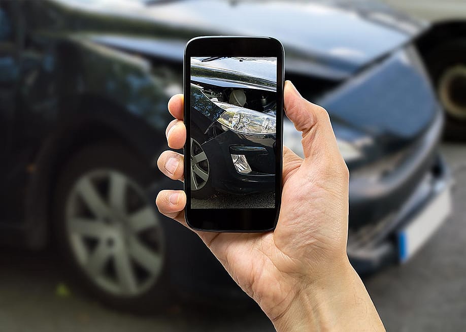 Person photographing passenger side headlight of damaged black car with smart phone for accident insurance. — cunaplus // Shutterstock