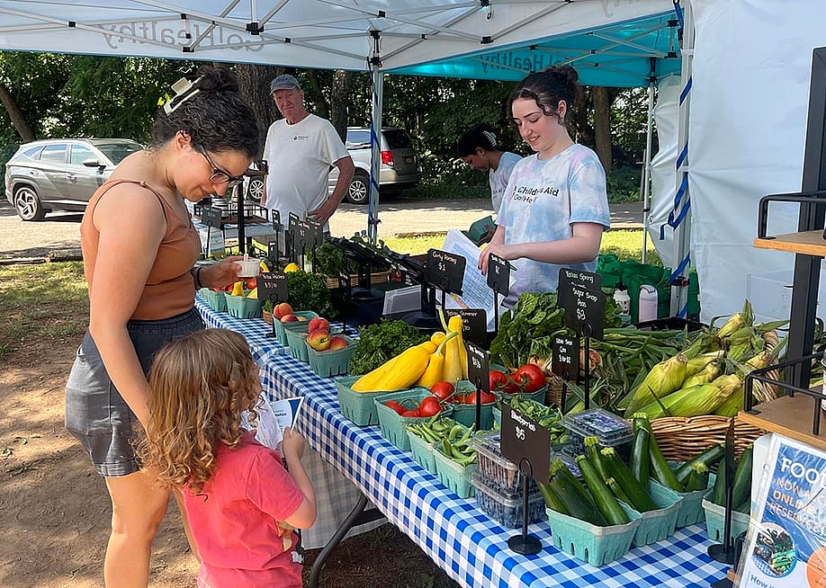 Ana Garcia, 41, and her 3-year-old son, Elliott, pick up a Food Box at a table full of colorful produce at the Goodhue Community Center on Staten Island — Eliza Fawcett // Healthbeat