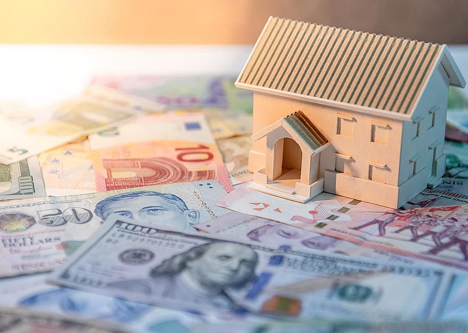 House model on various of international banknotes on the table. — Zephyr_p // Shutterstock