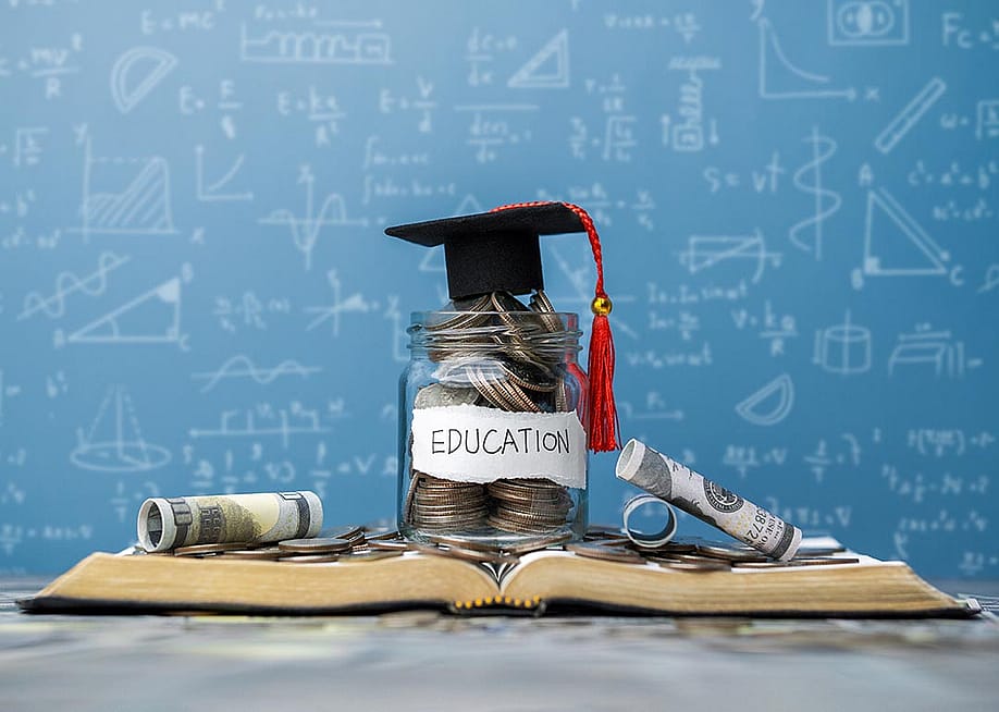 Photo illustration showing concept of college education cost with a jar of savings, a graduation cap, books and a blackboard with math in the background. — dee karen // Shutterstock