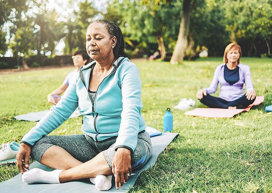 Three people in seated yoga poses on individual yoga mats on a green lawn, not sitting close together. — Nuva Frames // Shutterstock