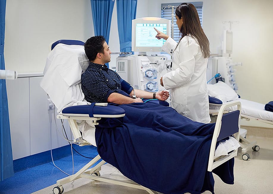 Patient sits getting hooked up to dialysis machine with nurse helping set up. — Yuri A // Shutterstock
