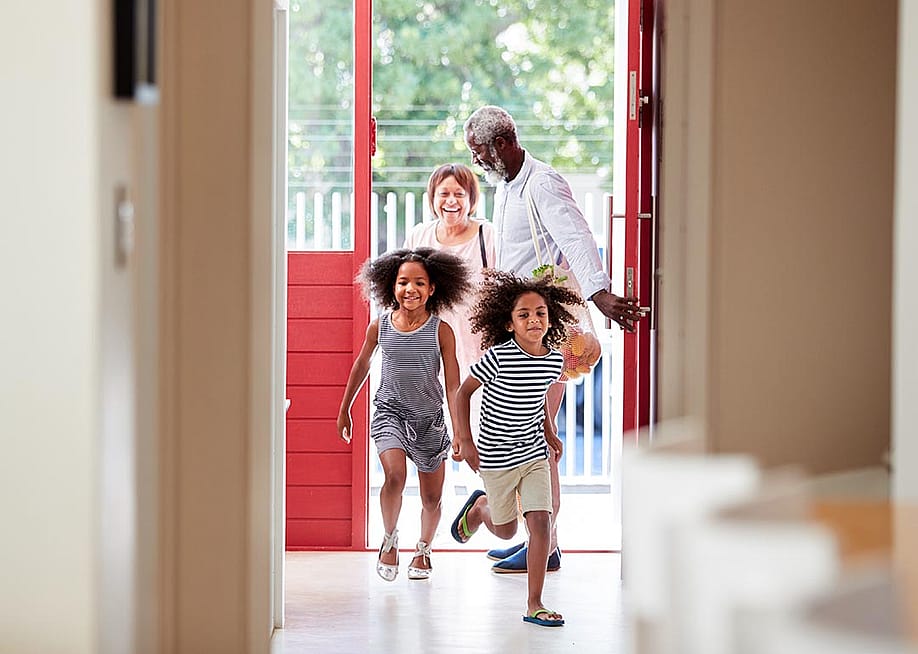 Two cute children with natural hair running into open door of house with grandparents in the background. — Monkey Business Images // Shutterstock