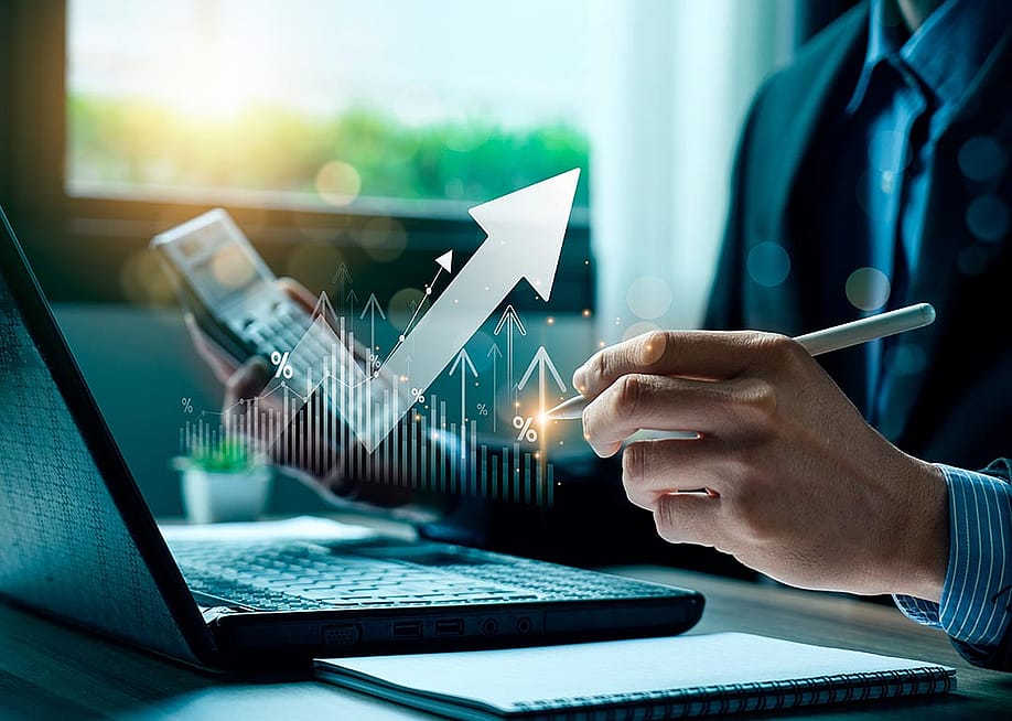 Person wearing a suit working on laptop and calculator, holding a pen with finance icons overlaid to symbolize money management. — Sutthiphong Chandaeng // Shutterstock