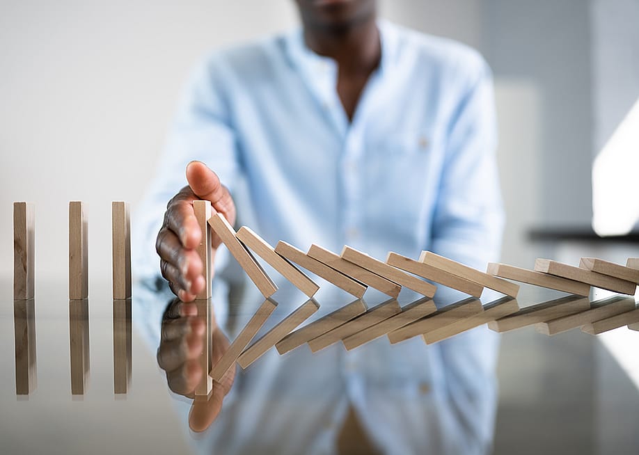 A businessman stopping a row of domino wooden bricks with his hand. — Andrey_Popov // Shutterstock