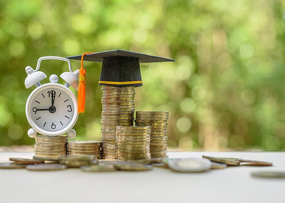 A clock and graduation cap on top of coins as a concept of student loans. — William Potter // Shutterstock