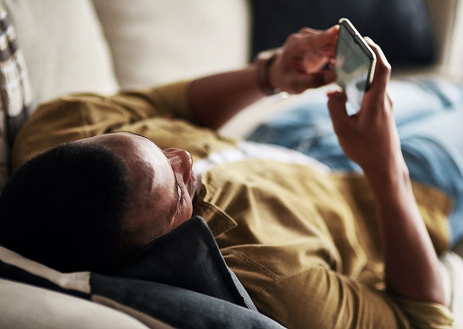 Young man relaxing on a couch at home while scrolling through social media on his phone. — PeopleImages.com - Yuri A // Shutterstock