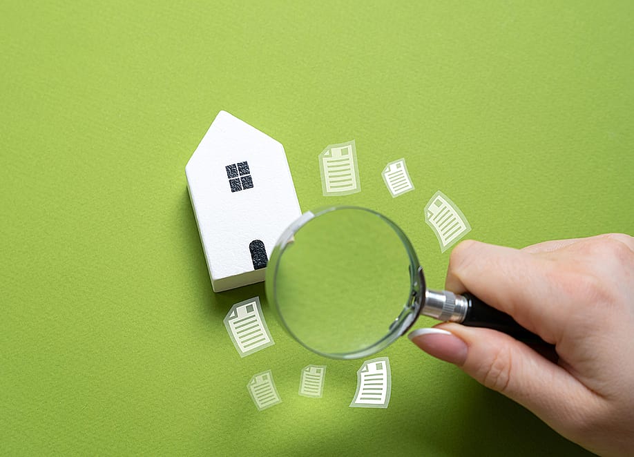A magnifying glass looking over a figure of a house on a green background. — Andrii Yalanskyi // Shutterstock