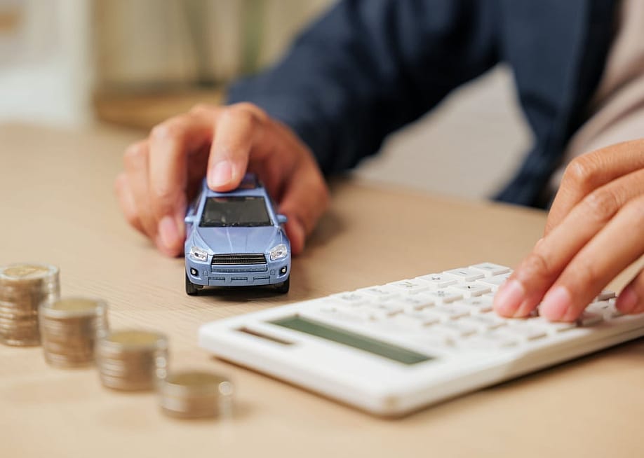 Calculator in hand as a person calculates car loan payments by a small car model and coins. — Sorapop Udomsri // Shutterstock
