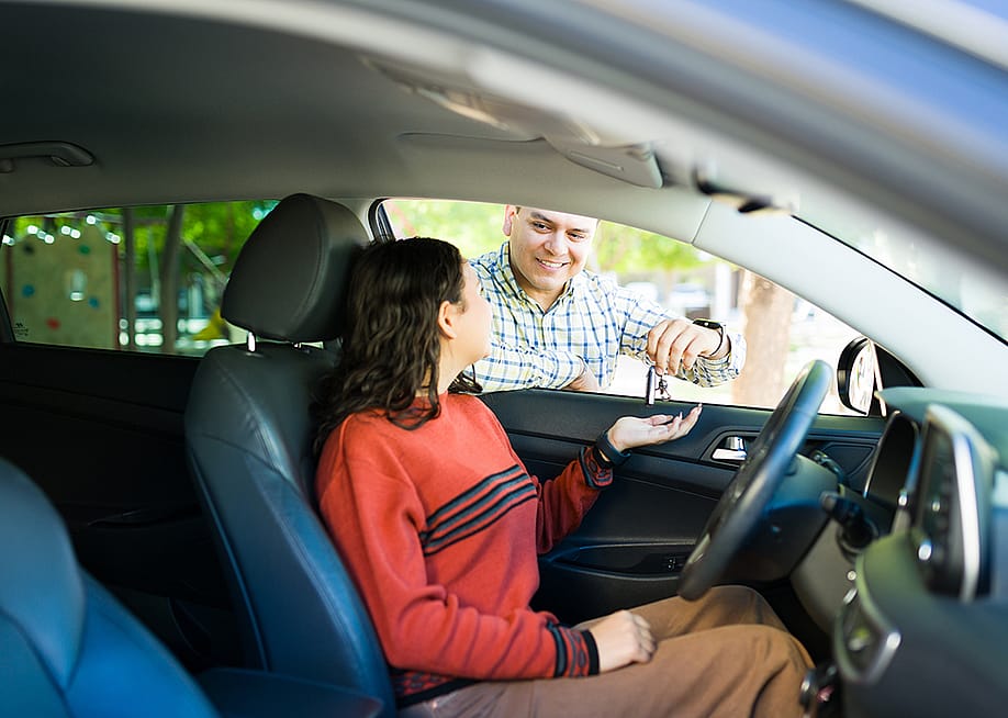 A teenage daughter inside a car receiving its keys from her proud dad. — antoniodiaz // Shutterstock