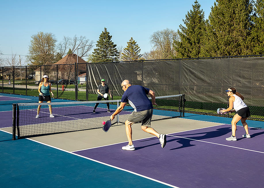 Two teams playing at a public park's pickleball court where a male player returns a volley at the net. — pics721 // Shutterstock