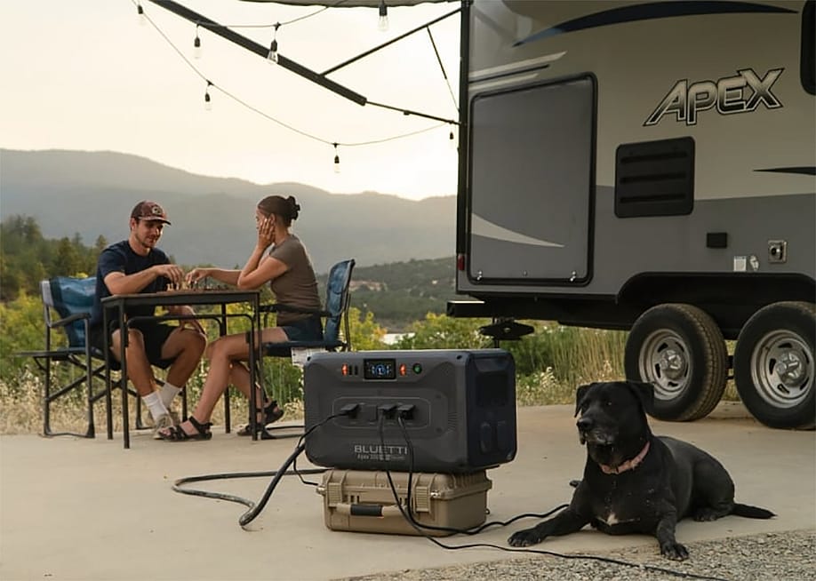 Couple at a table with a dog camping next to an RV. — BLUETTI