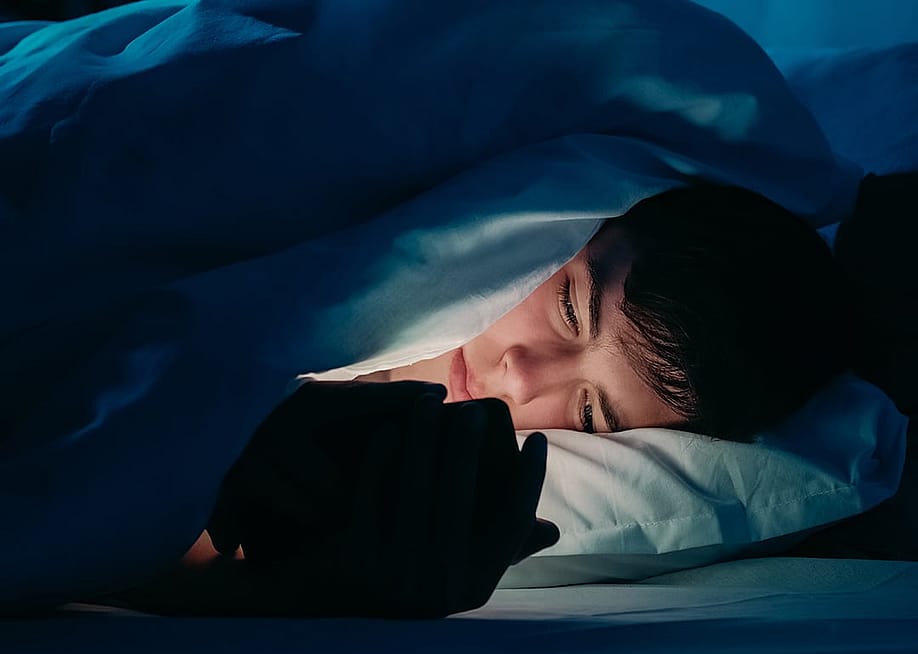 A male teenager using his smartphone under bedsheets at night. — Golubovy // Shutterstock