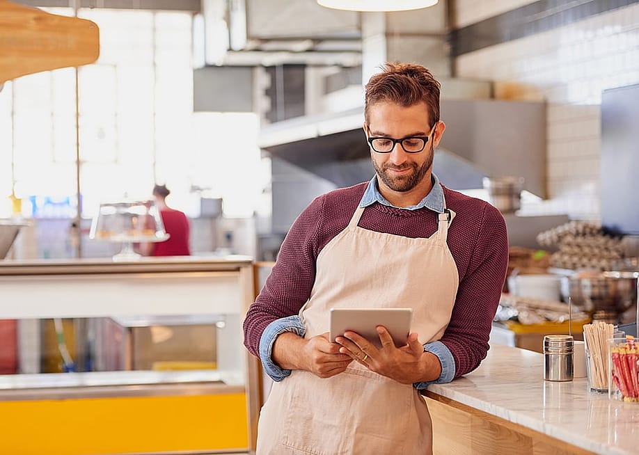 A coffee shop owner using a tablet inside the shop's kitchen. — PeopleImages.com - Yuri A // Shutterstock