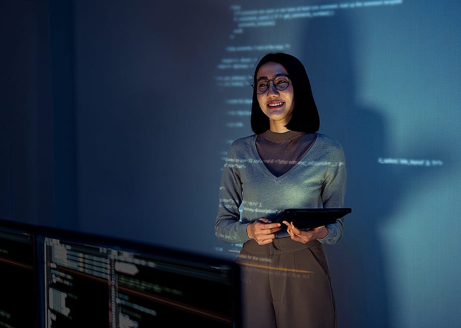A learning & development employee standing in front of a screen where software lessons are projected. — wee dezign // Shutterstock