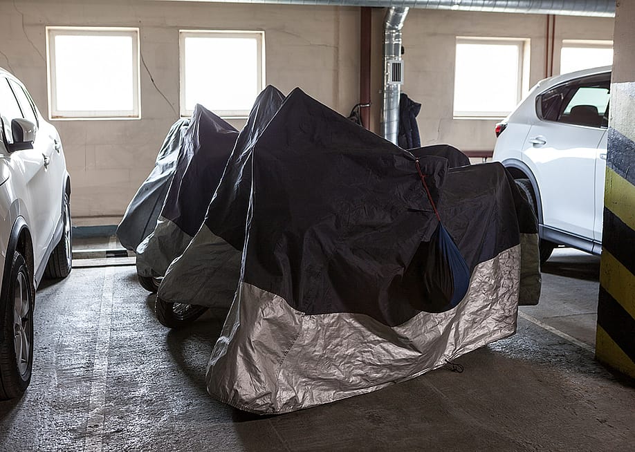 Motorcycles under dust protective covers parked in a row. — Kekyalyaynen // Shutterstock
