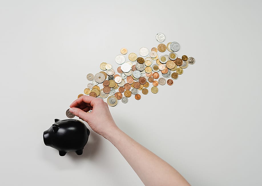 Coins being inserted into a black piggy bank. — Ichzan // Shutterstock